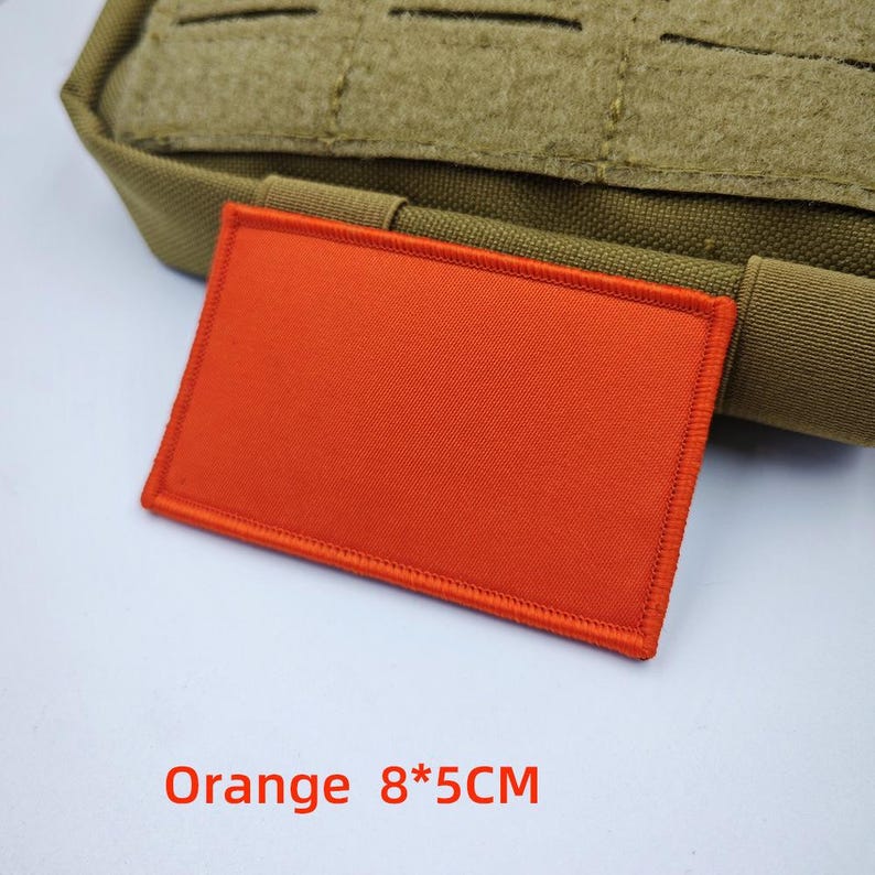 May include: Orange fabric patch with a stitched border. The patch is 8 centimetres by 5 centimetres.