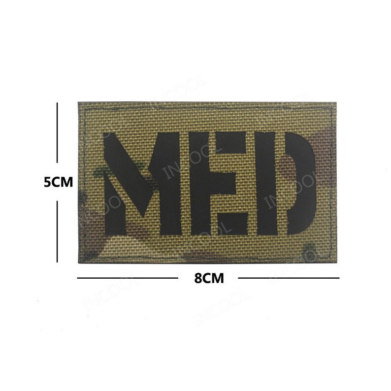 May include: A brown and green camouflage patch with the word "MED" in black lettering. The patch measures 8 cm by 5 cm.