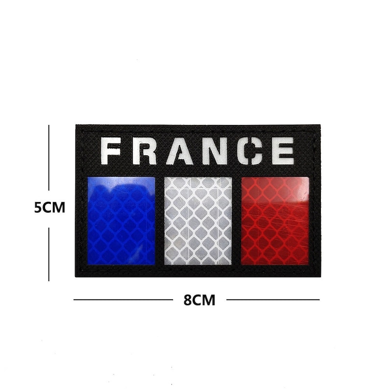 May include: A black patch with the word "FRANCE" in white letters and a reflective French flag design. The flag is made up of three vertical stripes: blue, white, and red. The patch measures 8 cm by 5 cm.