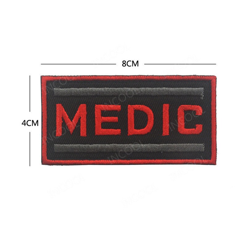 May include: A black embroidered patch with red lettering that says "MEDIC". The patch is 8 cm wide and 4 cm tall.