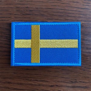 Può includere: Toppa ricamata raffigurante la bandiera svedese. La toppa rettangolare ha uno sfondo blu con una croce nordica gialla. I bordi sono bordati di blu. Per abbigliamento o accessori.