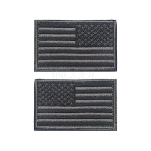 Pu&ograve; includere: Due toppe ricamate con la bandiera americana di colore nero. Le toppe sono rettangolari e hanno un contorno bianco.