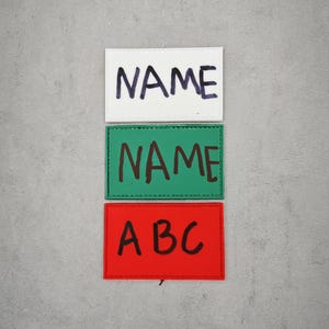 May include: Three rectangular name tags, one white, one green, and one red, each with the word "NAME" written in black marker. The red tag also has the letters "ABC" written in black marker.