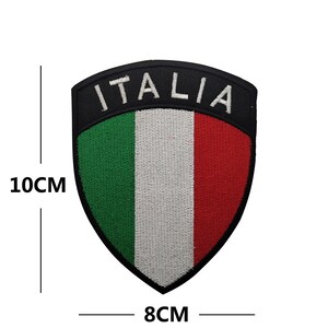 May include: An embroidered patch featuring the Italian flag in green, white, and red with the word "ITALIA" in white lettering on a black background. The patch is 8 cm wide and 10 cm tall.