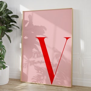 May include: A pink poster with a large red letter V in the center. The poster is framed in gold.