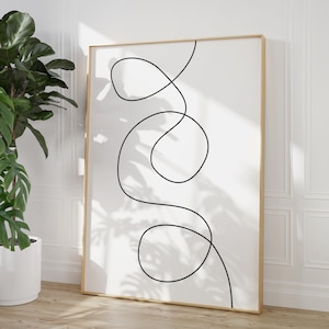 May include: A black and white abstract line art print in a gold frame. The print features a single continuous line that forms a series of loops and curves.
