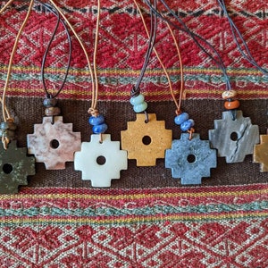 May include: Seven necklaces with leather cords and stone pendants. Each pendant is a four-pointed cross with a hole in the center. The stones are various colors, including green, pink, white, yellow, gray, brown, and orange.