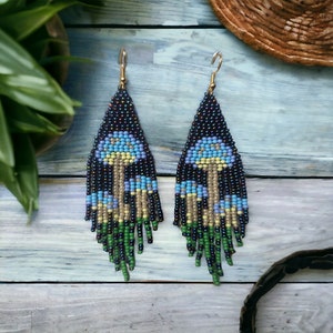 May include: A pair of long, beaded earrings with a fringe design. The earrings feature a pattern of blue and yellow mushrooms on a black background.