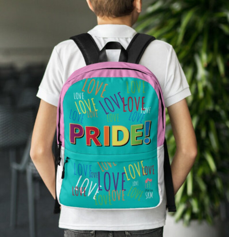 Op de afbeelding: Een turquoise rugzak met een roze rand en een regenboogkleurige "PRIDE!"-afbeelding. De rugzak is bedekt met het woord "LOVE" in verschillende kleuren en maten.
