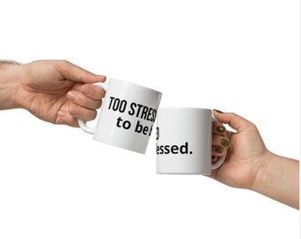 Può includere: Due tazze di ceramica bianca presentate in un brindisi. Una tazza recita "TOO STRESSED to be" e l'altra "blessed". Le tazze sono tenute da due mani su sfondo bianco.