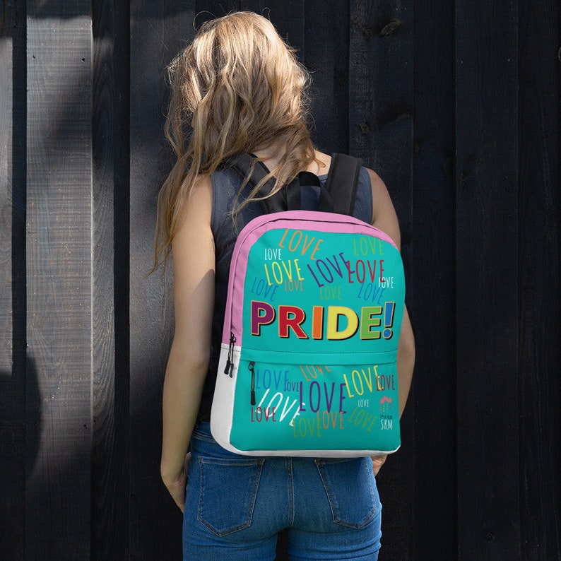 Op de afbeelding: Een turquoise en roze rugzak met het woord "PRIDE!" in regenboogkleuren en het woord "LOVE" herhaald in verschillende kleuren en maten.