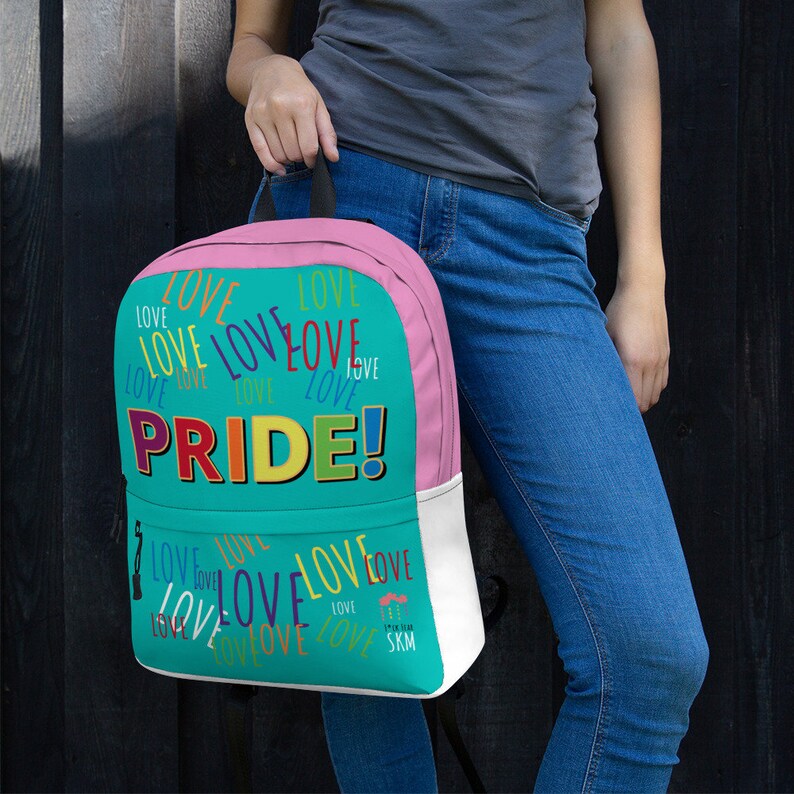 Op de afbeelding: Een turquoise en roze rugzak met het woord "PRIDE!" in regenboogkleuren. De rugzak is bedekt met het woord "LOVE" in verschillende kleuren en lettertypen.