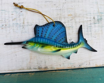 May include: A blue and green marlin fish ornament with a gold string for hanging. The fish is a popular nautical decoration.