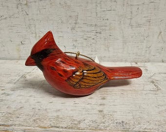 May include: A red cardinal bird ornament with brown and gold accents. The ornament is made of ceramic and has a loop for hanging.