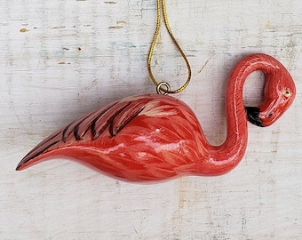 May include: Pink flamingo Christmas ornament with a gold string for hanging. The flamingo is made of ceramic and has a detailed design.