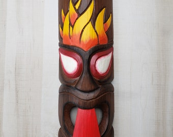 May include: A hand-carved wooden tiki mask with a dark brown finish. The mask features a green crown, flames, and a red tongue. The eyes are white with red outlines. The number "139" is at the bottom.