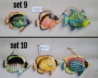 May include: Two sets of colorful fish ornaments, each set with three fish. The first set, labeled "set 9", features a green and black fish, a pink and orange fish, and a blue and green fish. The second set, labeled "set 10", features a black and white fish, a yellow fish, and a blue and green fish.