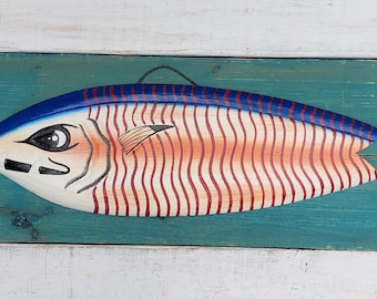 May include: A wooden fish wall decor painted in red, white, and blue. The fish has a stylized face and a striped body.