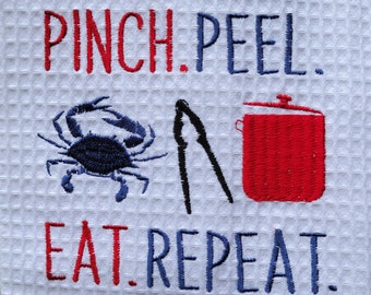 May include: White waffle-weave kitchen towel with embroidered text and graphics. The text reads "PINCH. PEEL. EAT. REPEAT." A blue crab, black seafood crackers, and a red pot are also embroidered on the towel.