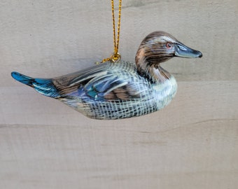 May include: A wooden duck ornament with blue and brown painted details, hanging from a gold string. The duck has a realistic appearance and is a great addition to any holiday decor.