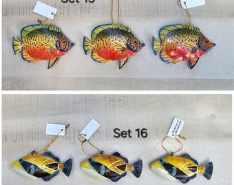 May include: Set of three colorful fish ornaments, painted in shades of yellow, red, blue, and green. The fish are hanging from gold strings and have a white tag with the text "Set 15".
