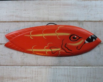 May include: A hand-painted wooden fish wall decor with a red body, yellow accents, and a black and white face with a toothy grin.