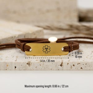 Puede incluir: Un brazalete de alerta m&eacute;dica de cuero marr&oacute;n con una placa de metal dorado grabada con el s&iacute;mbolo m&eacute;dico. La placa mide 3,5 cm de largo y 1 cm de ancho. El brazalete tiene una longitud de apertura m&aacute;xima de 22 cm.