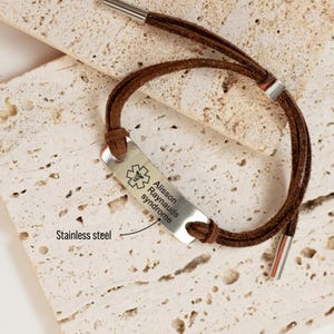 Puede incluir: Pulsera de alerta m&eacute;dica de cuero marr&oacute;n con una etiqueta de acero inoxidable grabada con el texto "Allisson Raynauds syndrome" y un s&iacute;mbolo m&eacute;dico.