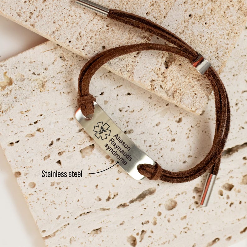 Puede incluir: Pulsera de alerta m&eacute;dica de cuero marr&oacute;n con una etiqueta de acero inoxidable grabada con el texto "Allisson Raynauds syndrome" y un s&iacute;mbolo m&eacute;dico.