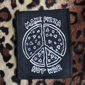 May include: Black fabric patch with white text and a peace sign design. The text reads "Make Pizza Not War" and the peace sign is made up of four pizza slices.