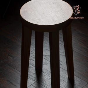 K&ouml;nnte beinhalten: Ein Hocker aus Holz mit einer runden Sitzfl&auml;che und drei Beinen. Der Hocker ist aus dunklem Holz gefertigt und hat eine nat&uuml;rliche Oberfl&auml;che.
