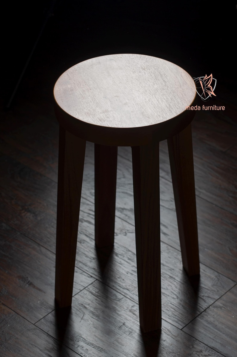 K&ouml;nnte beinhalten: Ein Hocker aus Holz mit einer runden Sitzfl&auml;che und drei Beinen. Der Hocker ist aus dunklem Holz gefertigt und hat eine nat&uuml;rliche Oberfl&auml;che.
