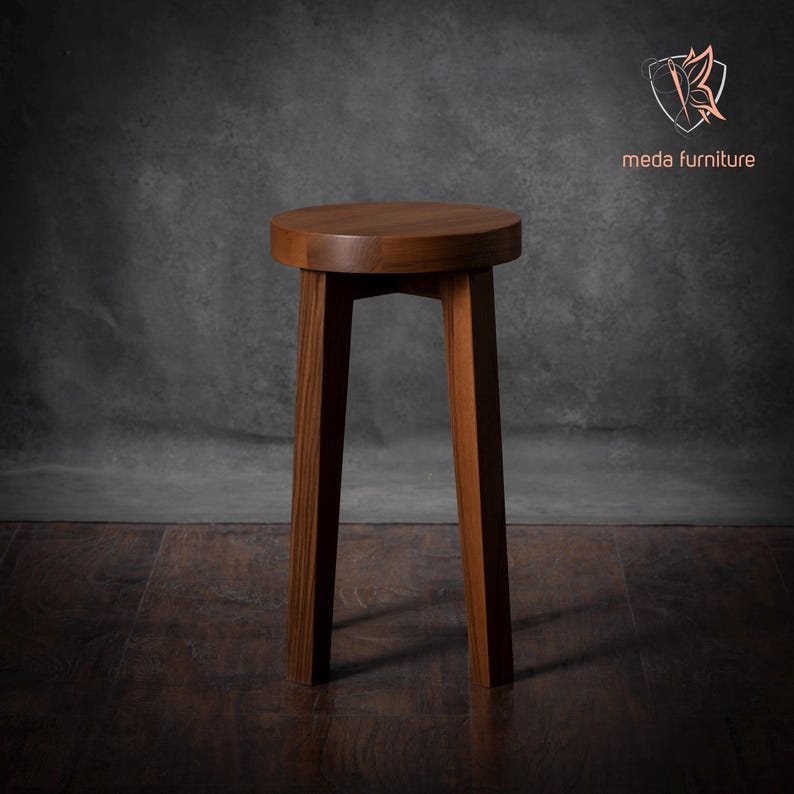 K&ouml;nnte beinhalten: Ein massiver Holzhocker mit runder Oberseite und vier Beinen. Der Hocker ist aus dunkelbraunem Holz gefertigt und hat ein schlichtes, modernes Design.