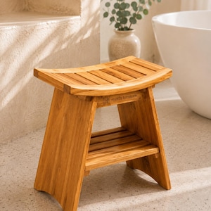 Puede incluir: Un taburete de ducha de madera marrón claro con un asiento curvo de listones y un estante de almacenamiento inferior. La estructura tiene patas inclinadas y el texto meda furniture está grabado en el riel de soporte frontal de madera.