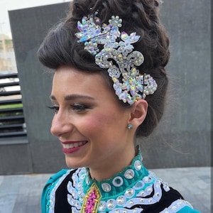 Op de afbeelding: Een vrouw met een groot, uitgebreid haarstuk met strass en een teal en zwarte jurk met strass.