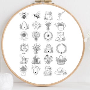 以下が含まれることがあります： 木製の丸い刺繍枠に白い布が張られ、黒い線画のグリッドが印刷されています。ミツバチ、巣箱、蜂蜜の瓶、花束、ラベンダー、ヒマワリ、じょうろ、長靴、そして「BEE HAPPY」と書かれた看板のイラストが描かれています。