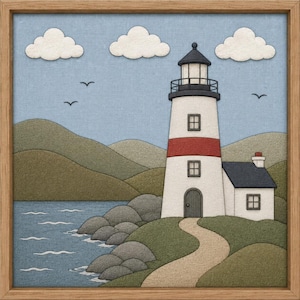 May include: A framed textile wall art piece depicting a coastal scene with a white lighthouse featuring a red stripe, a small adjacent house, rolling green hills, a blue sea with grey rocks, and three white clouds against a light blue sky.
