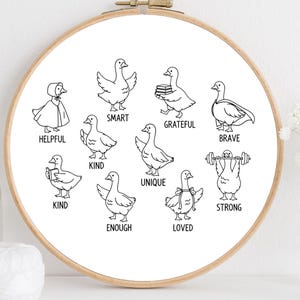 Può includere: Un telaio da ricamo rotondo con un'illustrazione in bianco e nero di anatre, ognuna raffigurante un tratto positivo come "utile", "intelligente" e "coraggioso". L'opera è su sfondo bianco.