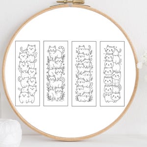 May include: Four black and white bookmarks with stacked cat illustrations are displayed inside a wooden embroidery hoop. Each bookmark features a different arrangement of cartoon cats. The background is white.