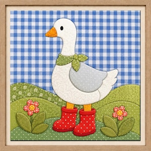 Op de afbeelding: Een ingelijst stoffen wandkunstwerk met een witte gans met een oranje snavel, die een groene sjaal met stippen en rode regenlaarzen met stippen draagt. De gans staat op een groen landschap met twee bloemen tegen een blauwe ruitjesachtergrond.