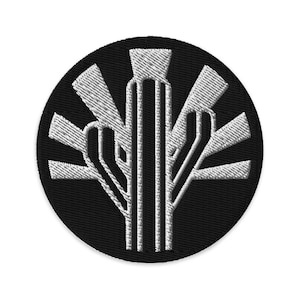 Puede incluir: Un parche redondo bordado en negro con un diseño blanco estilizado en forma de árbol. El diseño presenta un elemento vertical central con ramas angulares radiantes. Ideal para ropa o accesorios.
