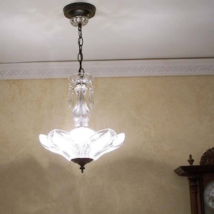 May include: A clear glass chandelier with a white frosted glass shade and crystal accents. The chandelier is hanging from a chain and has a black metal ceiling fixture.