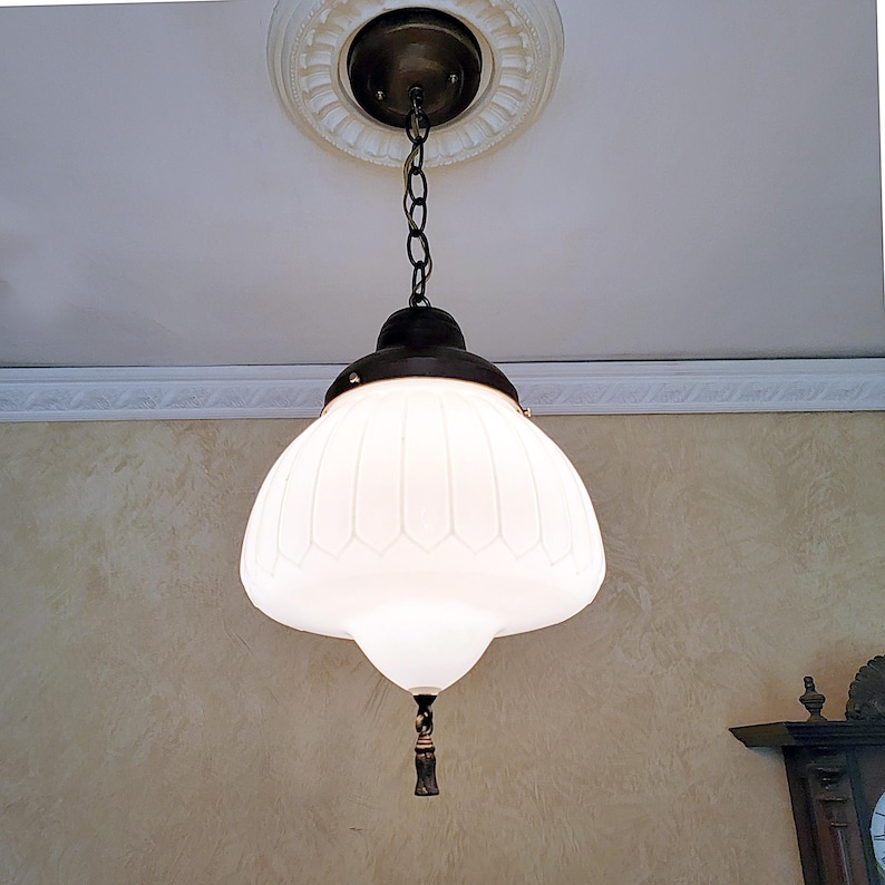 May include: A white glass pendant light fixture with a decorative, ribbed design hangs from a chain. The fixture has a dark brown metal base and a small, decorative finial.
