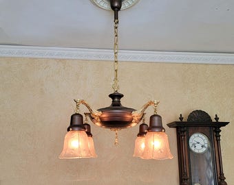 May include: A ceiling-mounted chandelier featuring a dark bronze finish with gold-toned accents. The fixture has a central hub suspended by a gold chain, with four downward-facing frosted glass shades that have a subtle star-like pattern.