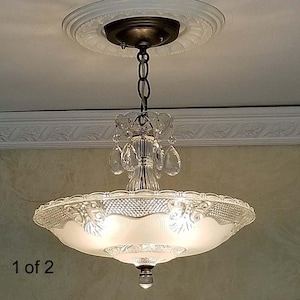 May include: A vintage-style ceiling light fixture with a frosted glass bowl shade and decorative crystal accents. The light hangs from a chain attached to a bronze-colored ceiling mount. The fixture has a classic, elegant design, suitable for interior lighting.