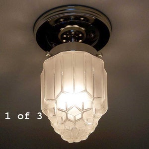 May include: A vintage ceiling light fixture with a frosted glass shade. The shade has a geometric design and is suspended from a chrome-colored base. The light is turned on, illuminating the room. The text "1 of 3" is visible.