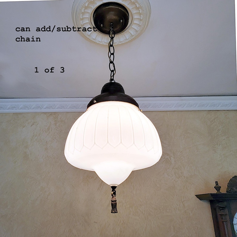 May include: A white glass pendant light fixture with a chain hanging from a ceiling medallion. The light fixture has a white frosted glass shade with a ribbed design and a small metal finial at the bottom.