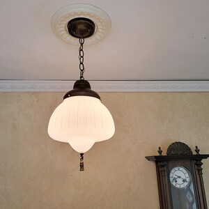 May include: A white glass pendant light fixture with a ribbed design hangs from a chain. The fixture has a bronze finish and a decorative finial.