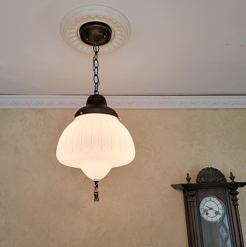 May include: A white glass pendant light fixture with a ribbed design hangs from a chain. The fixture has a bronze finish and a decorative finial.