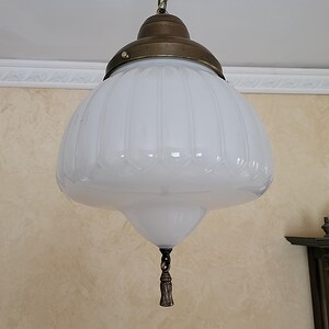 May include: A white glass pendant light fixture with a brass finish and a decorative tassel. The glass shade has a ribbed design.